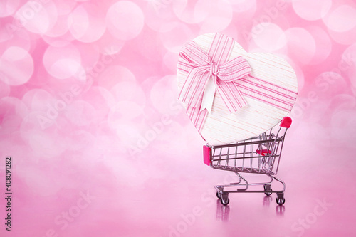 shopping cart with big gift with form of heart on pink with bokeh backgrounds