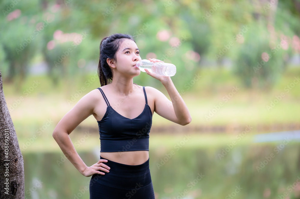Beautiful Asian women drink water before warming up to keep their muscles flexible Beautiful Asian women drink water before warming up to keep their muscles flexible
