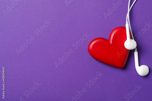 Modern earphones and red heart on purple background, flat lay with space for text. Listening love music songs © New Africa