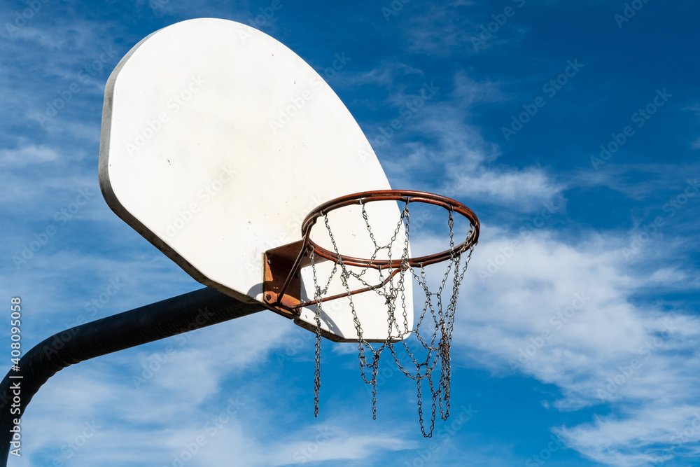 Old basketball hoop with a metal net against blue sky