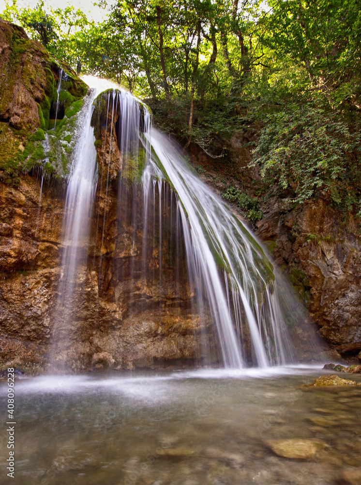 Obraz premium Waterfall Jur-Jur in winter, green moss and water, Crimea, Russia. White streams of water falling from a large stone in the forest, green moss around, green water