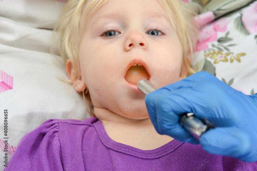 The doctor examines the oral cavity with a medical flashlight in a sick child. The doctor examines the oral cavity with a medical flashlight in a sick child.