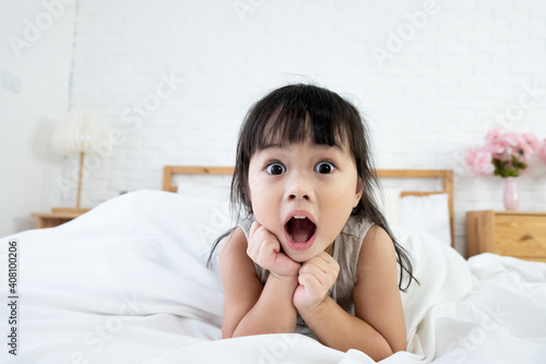 An asian toddler girl 3 years old waking up in bed with surprising expression.