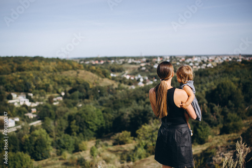 Mom with daughter in her arms on the mountain looking at the city. Rear view