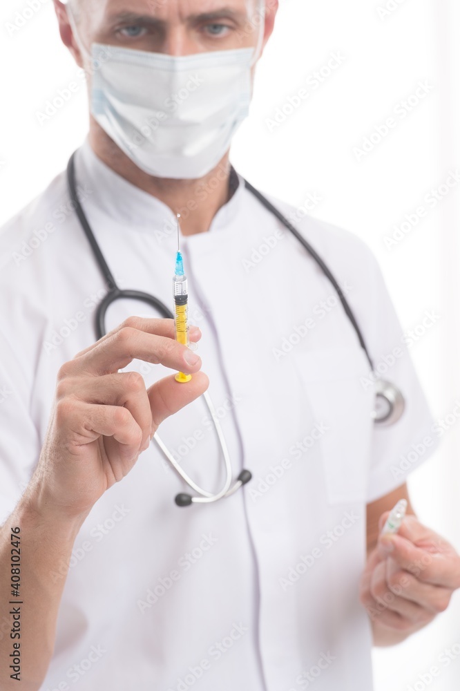 Covid-19 vaccine syringe with needle in hands of physician wearing medical face mask, shot