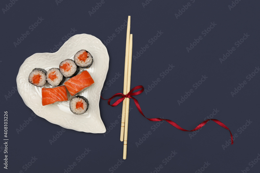 A heart-shaped plate with rolls and sushi sticks tied with a ribbon on a blue background.Layout. Concept: romantic creative presentation of rolls for Valentine's Day.Fast food A heart-shaped plate with rolls and sushi sticks tied with a ribbon on a blue background.Layout. Concept: romantic creative presentation of rolls for Valentine's Day.Fast food