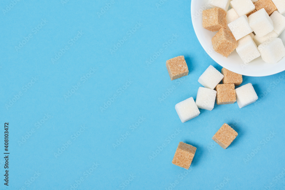 cubes of brown and white sugar sprinkled from a white bowl on a blue background cubes of brown and white sugar sprinkled from a white bowl on a blue background