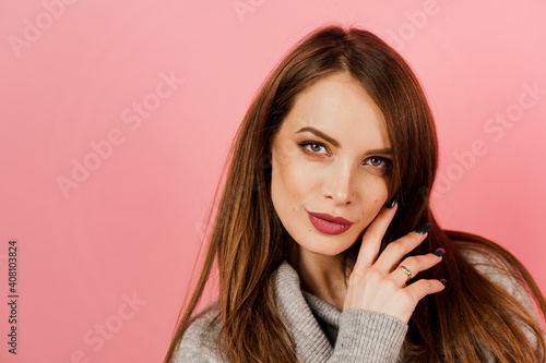 Close-up beauty portrait of a woman weared grey sweater on pink background. Professional model posing in studio. Lifestyle of caucasian happy girl