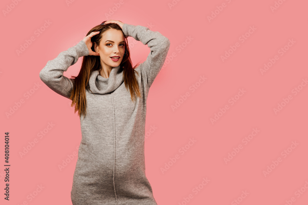 Pregnancy of a happy beautiful girl in a gray sweater on a pink background. Pregnant woman. Expectation of the child. Maternity leave. Pregnancy of a happy beautiful girl in a gray sweater on a pink background. Pregnant woman. Expectation of the child. Maternity leave.