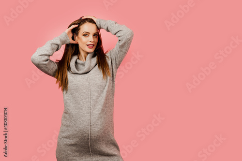 Pregnancy of a happy beautiful girl in a gray sweater on a pink background. Pregnant woman. Expectation of the child. Maternity leave. © Rabizo Anatolii