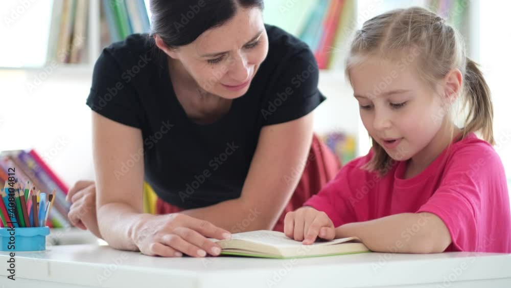 Little girl reading book with help of teacher in classroom Little girl reading book with help of teacher in classroom