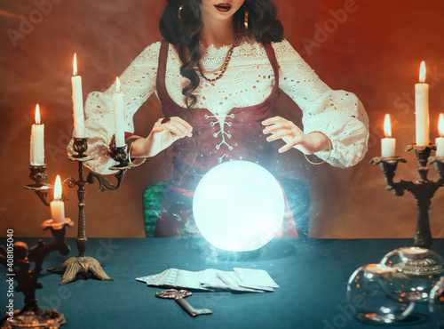 Fantasy retro women's hands close-up, witch feel energy magic of glowing crystal ball. dark gothic room. Photo of old art vintage astrology. Fortune teller woman reading future on magical tarot cards.