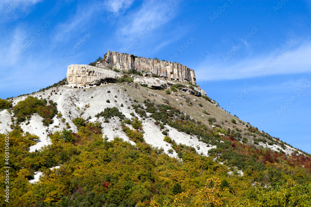 Tepe Kermen Cave City near Bakhchysarai in Crimea surrounded by colorful autumn forest under bright blue sky