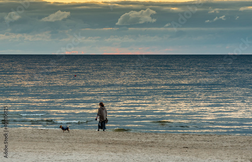 Young woman with a small dog during sunset on sandy beach of the Baltic Sea b...