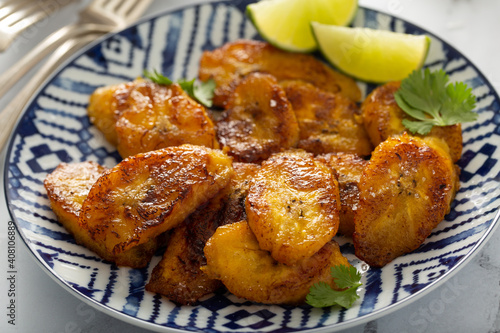 Fried caramelized plantains served with lime wedges and cilantro photo