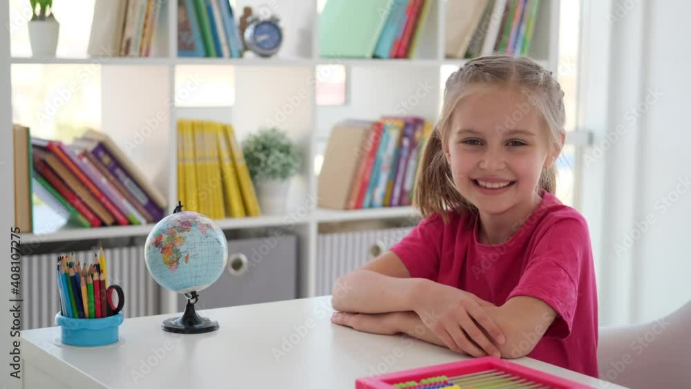 Smiling little girl sitting at school desk in bright classroom Smiling little girl sitting at school desk in bright classroom