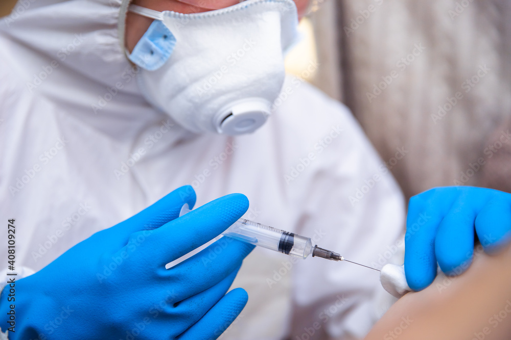 medicine, vaccination and healthcare concept - doctor wearing face protective medical mask for protection from virus disease with syringe doing injection of vaccine to male patient. medicine, vaccination and healthcare concept - doctor wearing face protective medical mask for protection from virus disease with syringe doing injection of vaccine to male patient.