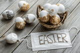 Easter composition with disposable protective mask and Easter eggs on a wooden surface.