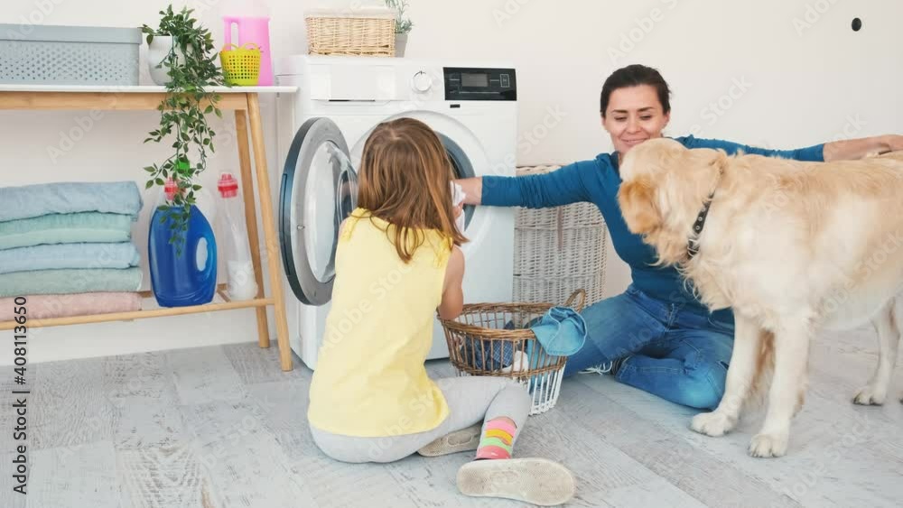 Little girl with woman and golden retriever dog washing clothes in machine at home Little girl with woman and golden retriever dog washing clothes in machine at home