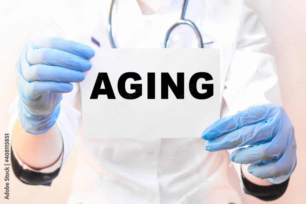 The doctor's blue - gloved hands show the word AGING - . a gloved hand on a white background. Medical concept. the medicine The doctor's blue - gloved hands show the word AGING - . a gloved hand on a white background. Medical concept. the medicine