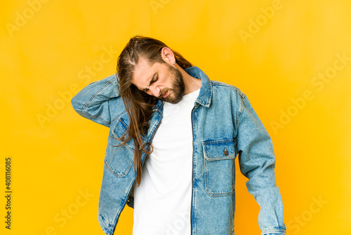 Young man with long hair look having a neck pain due to stress, massaging and touching it with hand. © Asier