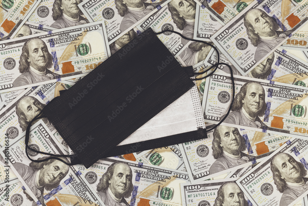 Protective mask on the background of 100 US dollars banknotes. The global financial crisis associated with the spread of coronavirus infection (COVID-19). Lockdown. Protective mask on the background of 100 US dollars banknotes. The global financial crisis associated with the spread of coronavirus infection (COVID-19). Lockdown.