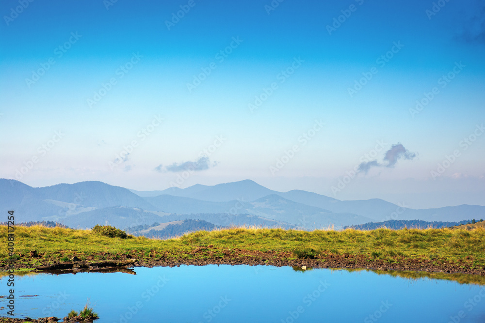 pond on the mountain meadow. beautiful summer landscape in morning light. grass on the hills. ridge in the distance
