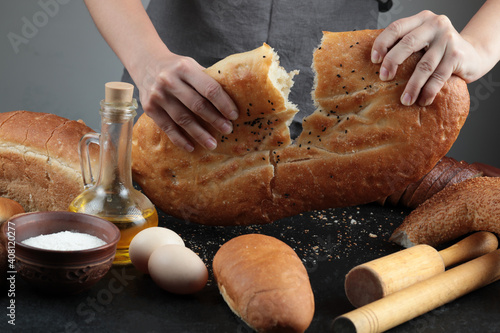 Woman cut bread into half on dark table with eggs, flour bowl and glass of oil