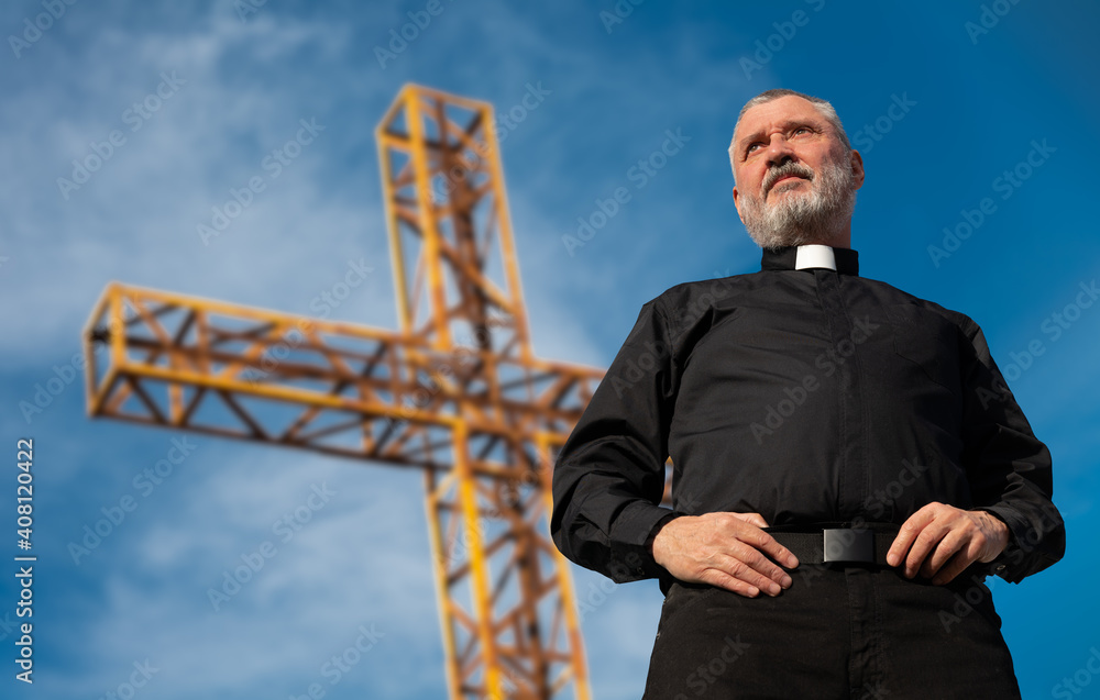 Φωτογραφία A priest in a black shirt and white clerical collar stands in front of the summit cross on Mount Muela near Orihuela in Spain