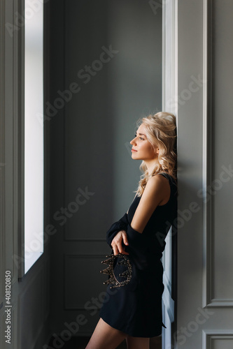 Elegant calm young blonde woman in black jacket, holding a crown in one hand.