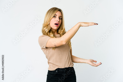 Young caucasian blonde woman shocked and amazed holding a copy space between hands.