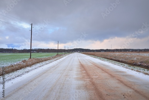 Snow-covered rural road through the field. Electricity line, transformer poles. Panoramic view from the car. Colorful clouds, dramatic sunset sky. Off-road, logistics, winter tires, remote village photo