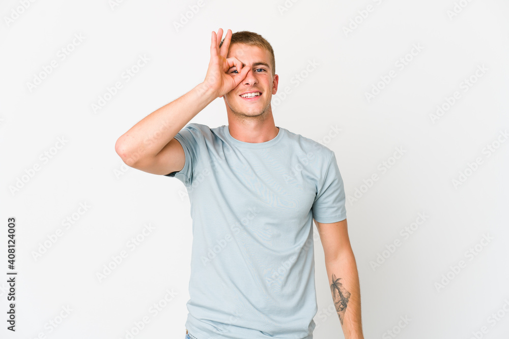 Fototapeta premium Young caucasian handsome man excited keeping ok gesture on eye.
