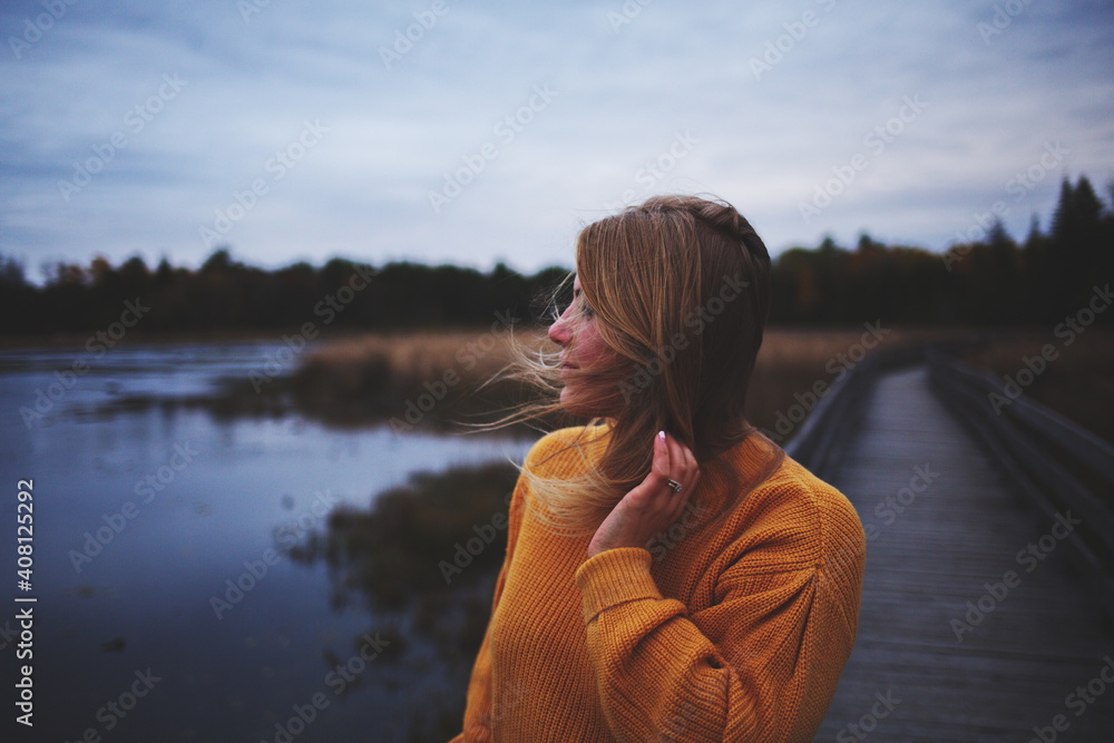 Woman in an orange sweater looking across the water at a local park in Ontario, Canada during the autumn season. Woman in an orange sweater looking across the water at a local park in Ontario, Canada during the autumn season.