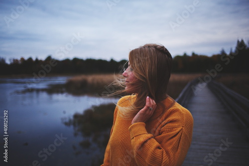 Canvas Print Woman in an orange sweater looking across the water at a local park in Ontario, Canada during the autumn season