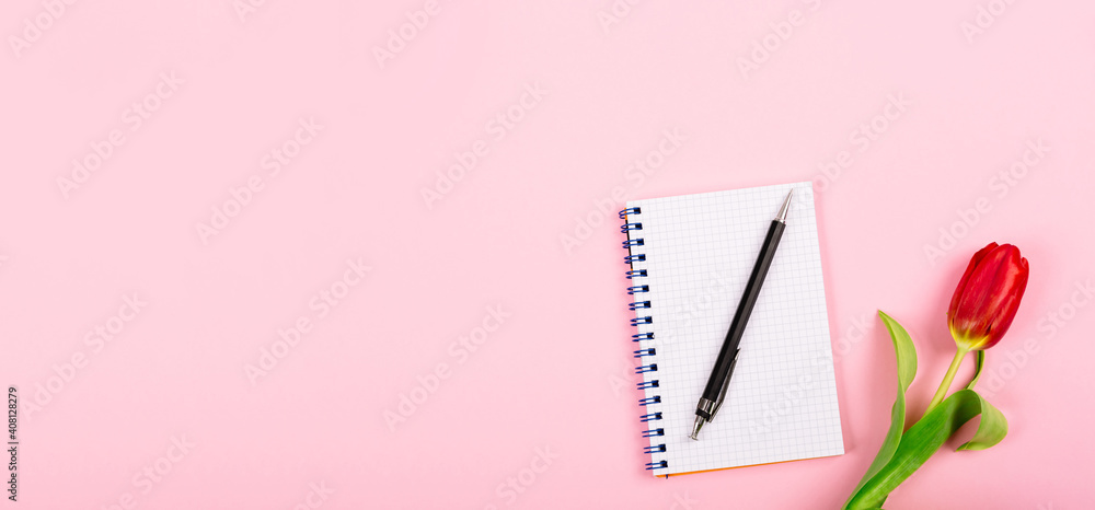 Open spiral notepad with pen and red tulip on pink desk background. Template for advertising or visualization of blog with copy space for text. Business holiday card. Certificate mockup. Top view