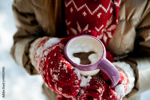 A mug of delicious cocoa with marshmallow in children's hands on a winter day.