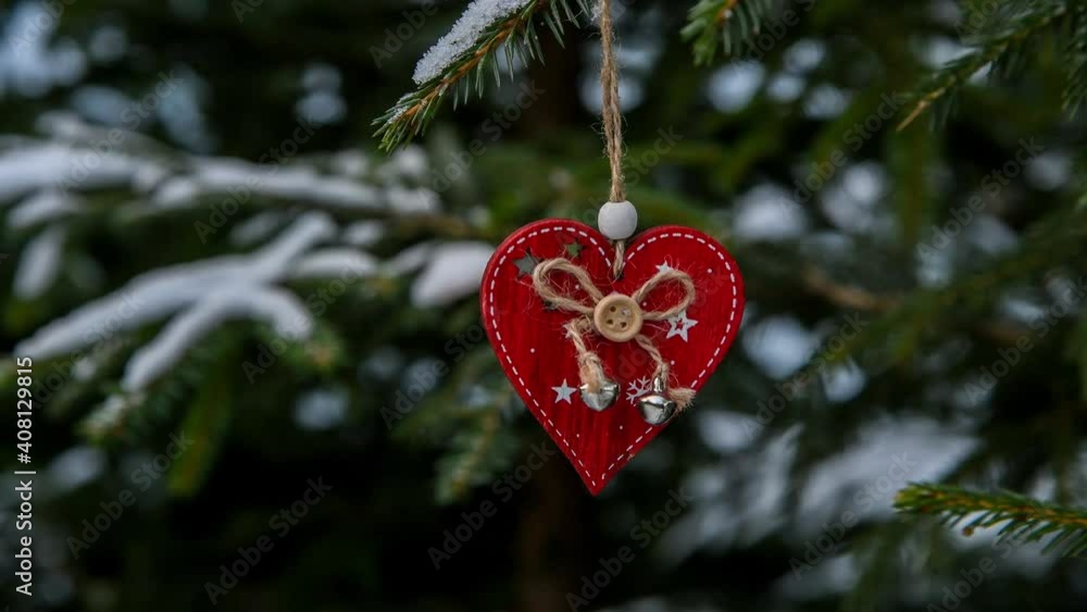 Wooden Сhristmas ornament in the shape of red heart hangs on the Christmas tree branch covered with snow. Frosty day. Romantic Christmas theme. Wooden Сhristmas ornament in the shape of red heart hangs on the Christmas tree branch covered with snow. Frosty day. Romantic Christmas theme.