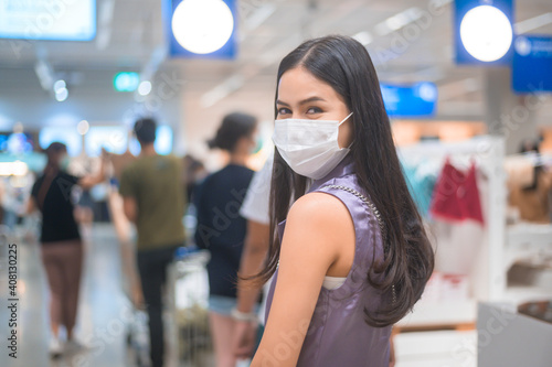 young woman wearing a surgical mask waiting in line near cashier counter in supermarket, covid-19 and pandemic concept