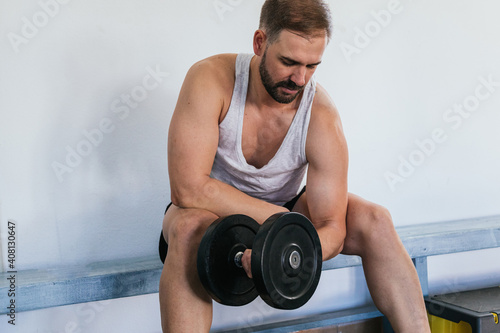 Man doing biceps exercises with dumbbells at the gym. sitting on a bench. health and wellness concept.