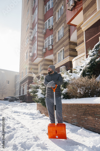 A young man clears the snow in front of the house on a sunny and frosty day. © Andrii