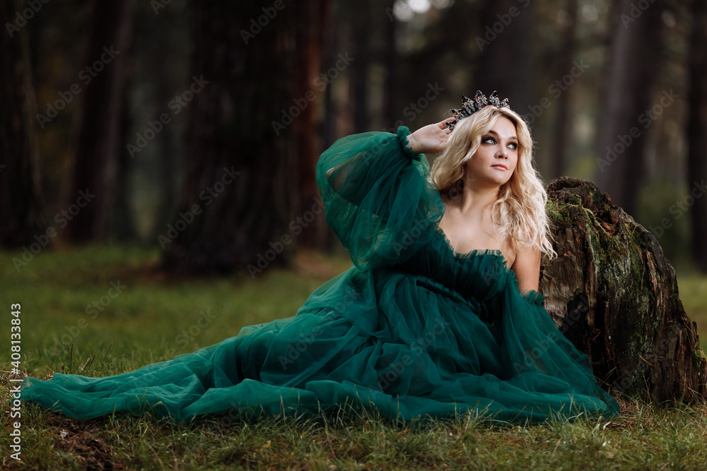 A beautiful blonde young woman in a long green dress and a diadem on ...