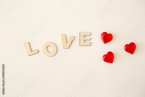 Wooden letters with the inscription of the word "Love" on a white background and next to a three small red hearts