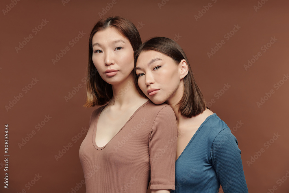 Gorgeous girl of Asian ethnicity keeping head on shoulder of her twin sister Gorgeous girl of Asian ethnicity keeping head on shoulder of her twin sister