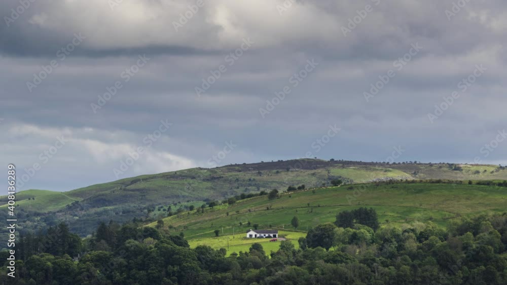 Time lapse of rural agriculture landscape with a farmhouse on a hillside with forest in the foreground on a cloudy summer day in Ireland. Time lapse of rural agriculture landscape with a farmhouse on a hillside with forest in the foreground on a cloudy summer day in Ireland.