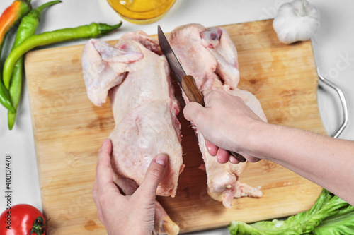 Woman hand cutting raw whole chicken with knife on wooden chopping board