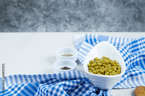 Boiled green peas in a white bowl on a white background with spices and a tablecloth