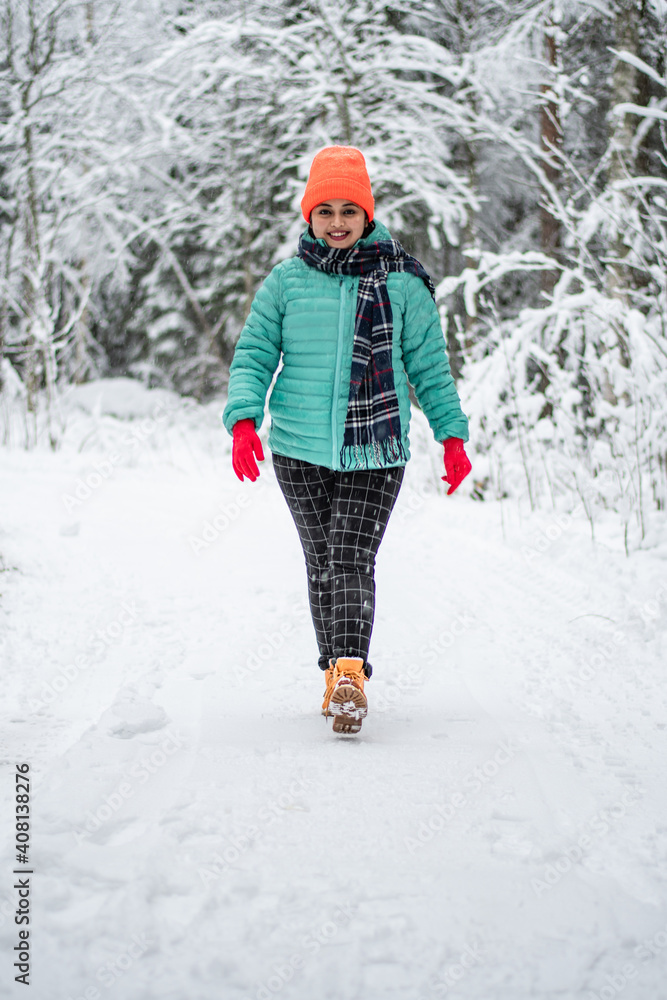 A beautiful young woman in a winter wonderland enjoying the snow fashion walk wearing colourful jacket and red cap