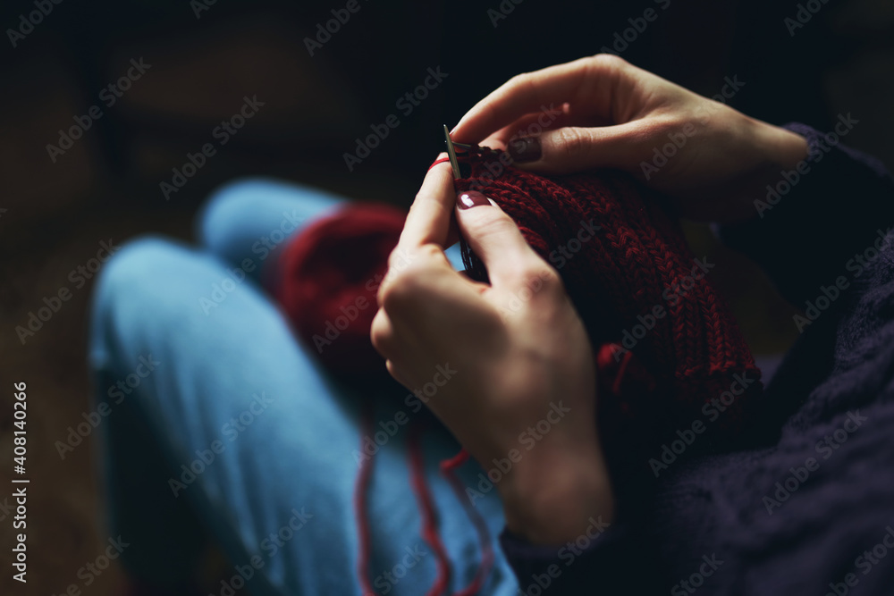 Female hands knitting with red yarn.