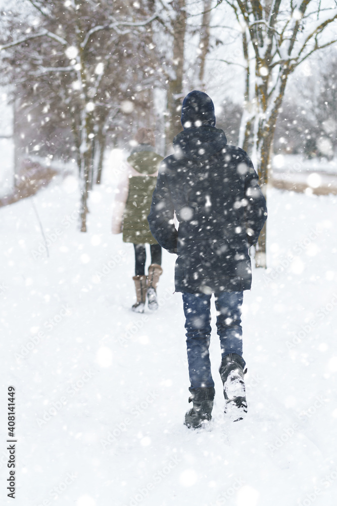 two people walk on a snow-covered path in winter, a teenage boy and a girl, a snowstorm